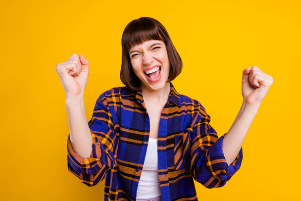 Portrait of attractive lucky overjoyed cheerful girl wearing plaid shirt rejoicing isolated over bright yellow color background - Photo, image