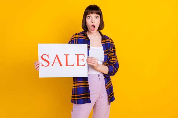 Portrait of attractive amazed girl holding in hands sale board isolated over bright yellow color background - 写真・画像