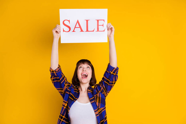 Portrait of attractive cheerful girl holding in hands rising up sale board wow isolated over bright yellow color background - Φωτογραφία, εικόνα