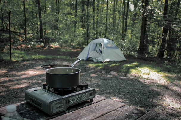 Black Moshannon State Park, Pennsylvania, USA - June 10 2020: Food is being cooked on a portable gas stove in a campgrounds at a campsite. - Фото, зображення