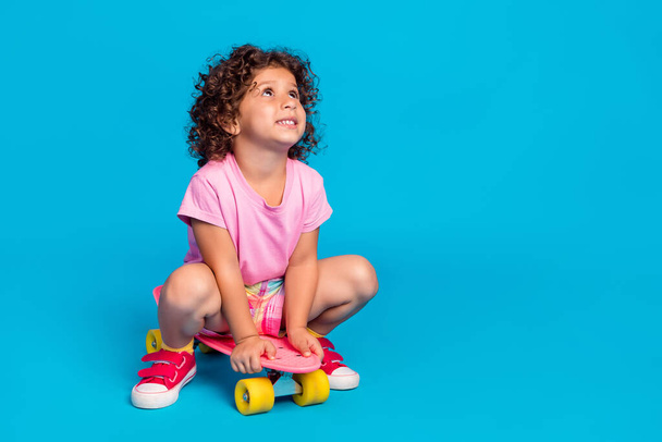 Portrait of attractive dreamy cheerful wavy-haired girl riding skate copy space isolated over bright blue color background - Foto, Imagen