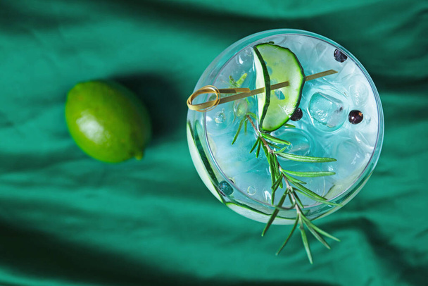 Glas fris koud water met ijs, komkommerschijfjes en kalk op groene ondergrond - Foto, afbeelding