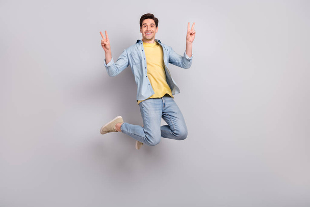 Photo of pretty cheerful guy dressed denim shirt showing two v-signs jumping high isolated grey color background - Fotografie, Obrázek