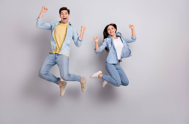 Photo of lucky brother sister wear jeans shirts rising fists jumping hign isolated concrete grey wall background - Foto, Bild