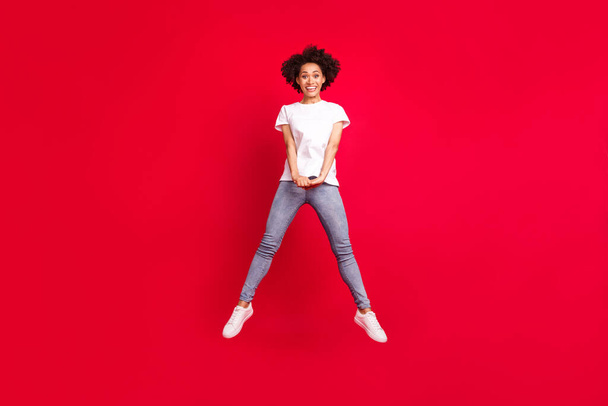 Full length body size photo smiling curly woman jumping up happy isolated vivid red color background - Photo, Image