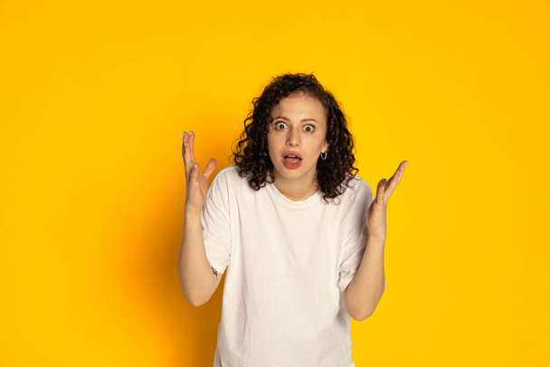 One surprised young beautiful girl in white t-shirt wondering isolated on yellow background. Concept of emotions - Foto, Imagen