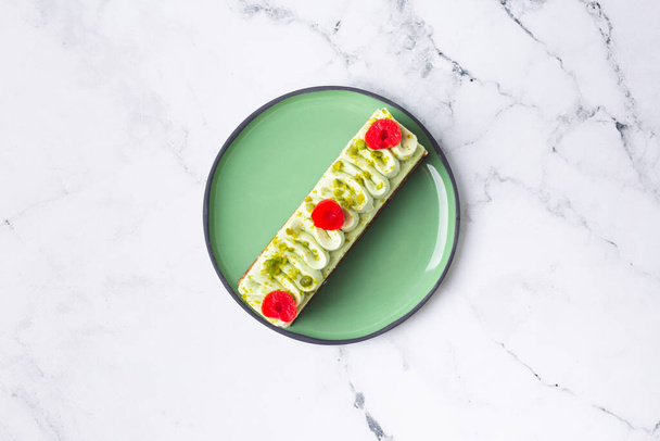 Pastry cake dessert decorated with green cream, cherry and pistachio on marble background - Фото, изображение
