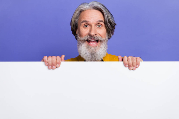 Portrait of attractive cheerful gray-haired man showing copy empty space ad isolated over bright violet purple color background - Фото, изображение
