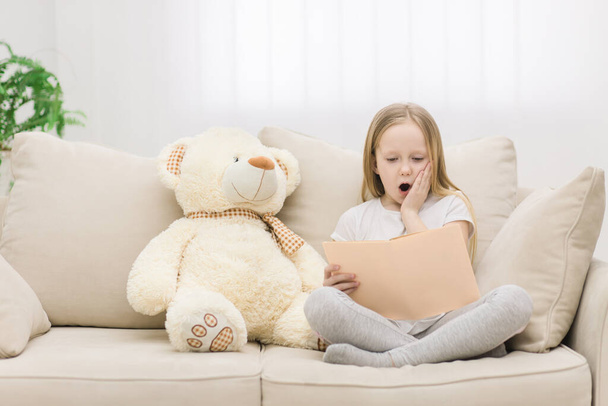 Photo of blond girl reading a book to her toy plush friend. - 写真・画像