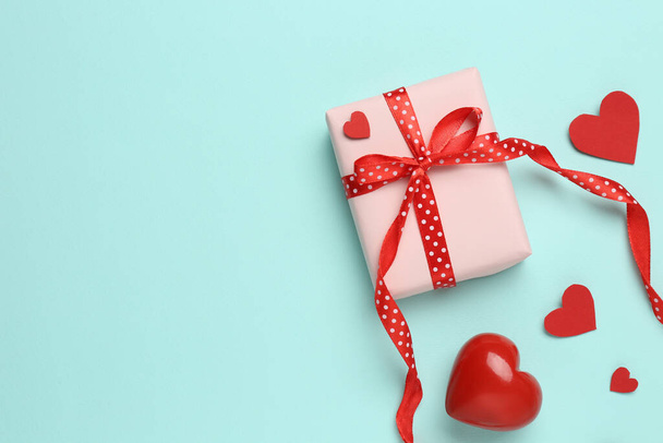 Gift box with decorative red hearts on turquoise background, flat lay. Space for text - Fotó, kép