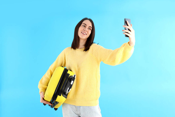 Kobieta z torbą podróżną robi selfie na niebieskim tle - Zdjęcie, obraz