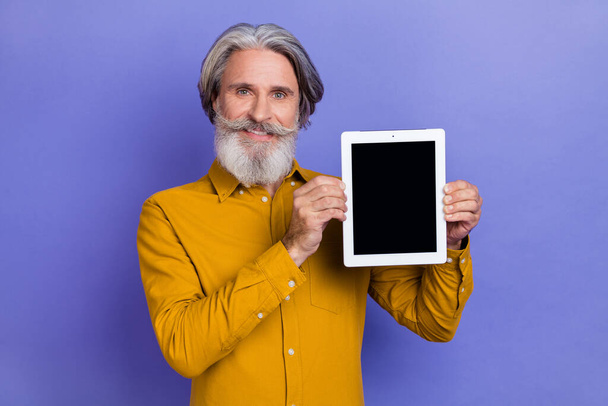 Portret van aantrekkelijke vrolijk grijs-harige man met tablet kopieerruimte geïsoleerd over heldere paarse kleur achtergrond - Foto, afbeelding