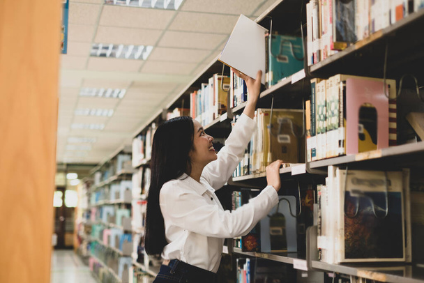 Junge asiatische Frauen suchen auf den Tischen und Gängen der Universitätsbibliotheken nach Büchern und Lesebüchern, um ihr akademisches und pädagogisches Selbst zu erforschen und zu entwickeln.. - Foto, Bild