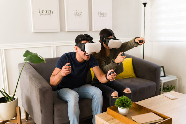 Szczęśliwy mężczyzna i kobieta za pomocą wirtualnej rzeczywistości gogle i joysticks podczas korzystania z gry wideo symulator w salonie  - Zdjęcie, obraz