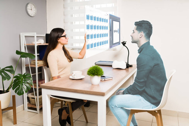 Jeune femme intelligente parlant avec un homme virtuel dans la métaverse à son bureau en utilisant des lunettes de réalité augmentée  - Photo, image