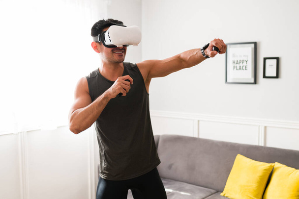 Happy man using the latest technology to work out. Smiling young man enjoying exercising with virtual reality goggles - Foto, Imagem