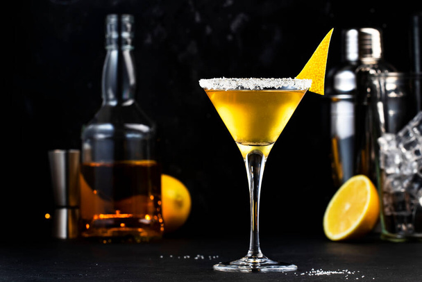 Sidecar classic alcoholic cocktail with cognac, liqueur, lemon juice and ice. Black background, bar tools, night atmosphere - Photo, image