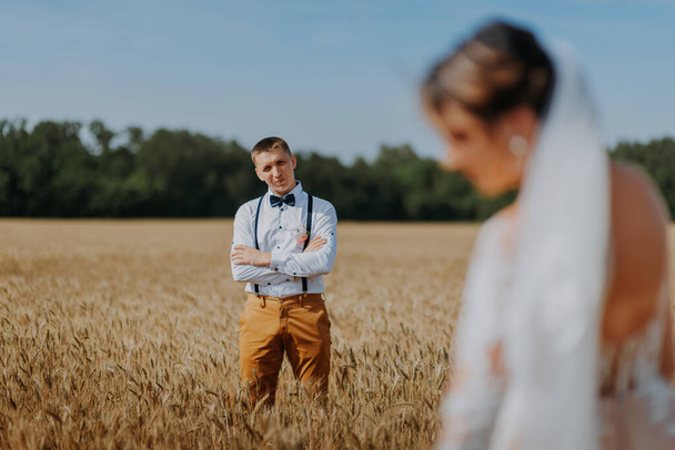 fashionable and happy wedding couple at wheat field at sunny day. Bride and groom kissing in a wheat field. Young beautiful wedding couple hugging in a field with grass eared. - Foto, Bild