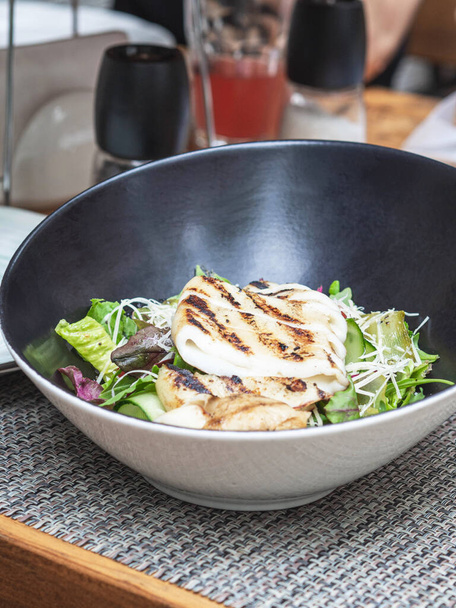 Grilled squid, lettuce and cheese salad in black ceramic bowl on table in restaurant - Photo, Image