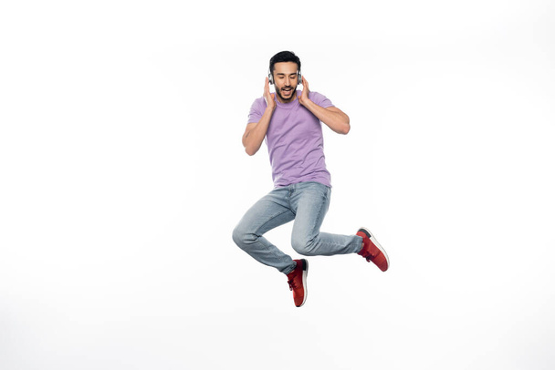 hombre positivo en auriculares inalámbricos levitando sobre blanco - Foto, imagen