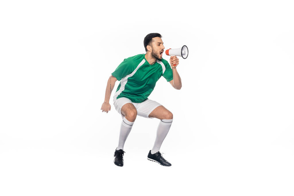 jonge voetballer in uniform springen en schreeuwen in luidspreker geïsoleerd op wit  - Foto, afbeelding