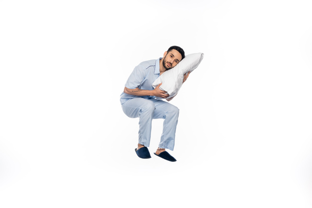 bearded man in pajamas levitating with pillow on white  - Foto, imagen