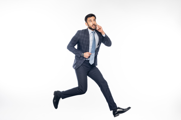 pensive businessman in suit jumping and talking on smartphone on white  - Photo, Image
