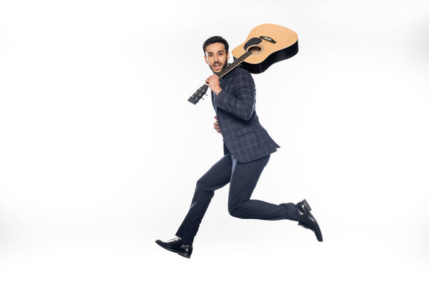 happy businessman in suit jumping with acoustic guitar on white  - Valokuva, kuva