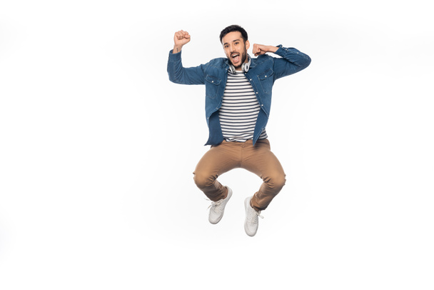 hombre feliz con auriculares inalámbricos levitando y animando aislado en blanco  - Foto, imagen