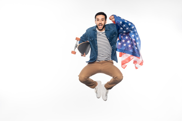 hombre feliz levitando mientras sostiene longboard y bandera americana en blanco - Foto, imagen