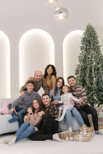 Μια μεγάλη κομψή οικογένεια την παραμονή των Χριστουγέννων. Πορτρέτο της μεγάλης οικογενειακής συγκέντρωσης. Νέοι παππούδες και γιαγιά με εγγονή, εγγονό, αδέλφια, εγγόνια που κάθονται στο πάτωμα - Φωτογραφία, εικόνα