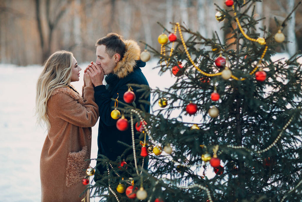 Молода доросла пара прикрашає ялинку в зимовому лісі. Концепція святкового святкування новорічної сосни
. - Фото, зображення