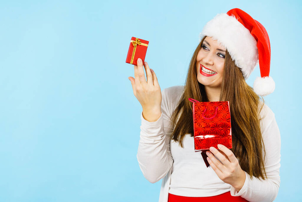 Christmas gifts. Happy woman wearing santa claus hat holding present red bag and small gift box with jewelery, on blue - Foto, Bild