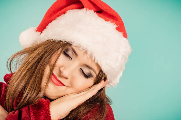 Tired woman wearing santa hat gesturing sleep gesutre with her hands. Adult female being sleepy, ready to take a nap. Christmas time. - Фото, изображение