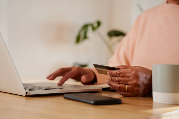 Hands of elderly multi-ethnic female making online payment on laptop, sitting at kitchen counter.  - Фото, изображение