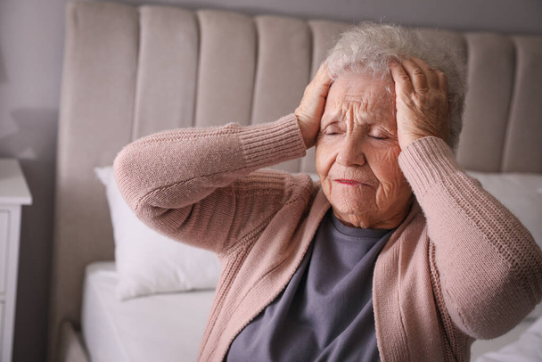 Senior woman with headache in bedroom at home - Foto, imagen