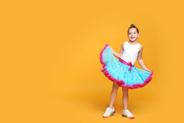 Cute little girl in tutu skirt dancing on yellow background. Space for text - Foto, imagen