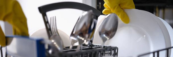 A sárga kesztyűs ember tiszta edényeket vesz ki a mosogatógépből. - Fotó, kép