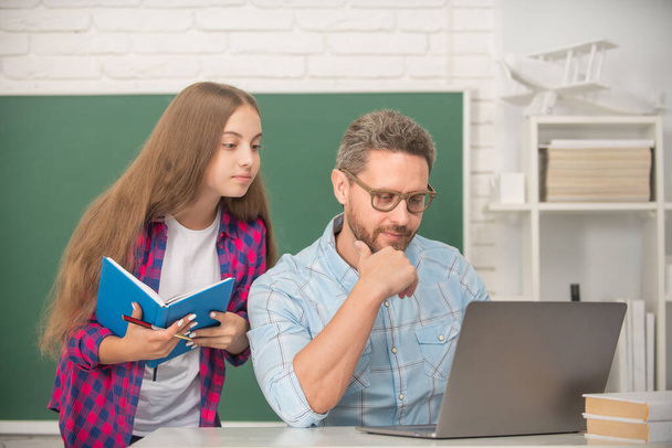 niño y papá atentos sentados en el aula con copybook y computadora en pizarra, trabajo escolar - Foto, imagen