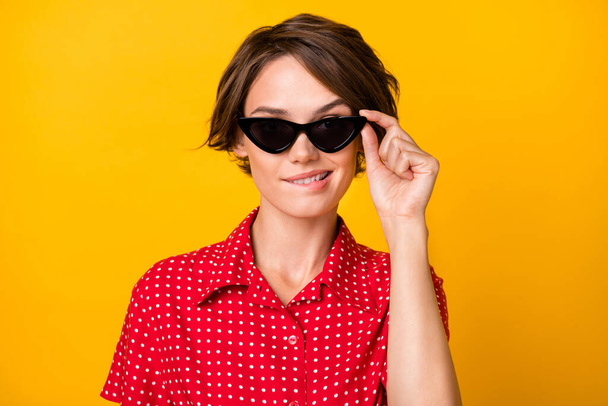 Portrait of charming thoughtful girl teeth biting lip hand touch sunglass isolated on yellow color background - Foto, afbeelding