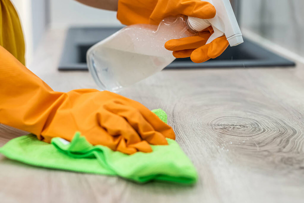 Close up on human hands in yellow gloves with spray cleaning wooden surface - Photo, Image