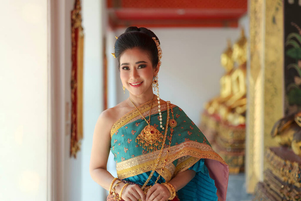 Portrait Asian women smiling and wearing Thai national costumes are inside temples to worship Buddha with flower garlands on important religious days for Thai people. - Photo, Image