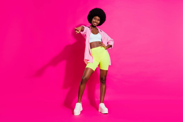 Photo of adorable pretty dark skin woman dressed crop top smiling dancing pointing finger you isolated pink color background - Foto, imagen