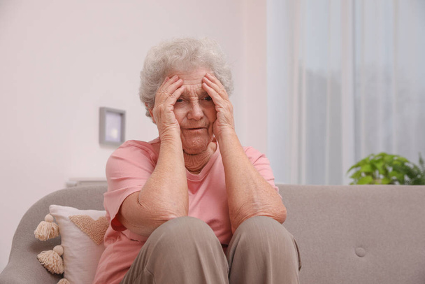 Mujer mayor con dolor de cabeza sentada en el sofá en casa - Foto, Imagen