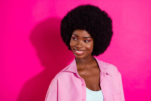 Photo of shiny adorable dark skin lady wear casual shirt looking empty space smiling isolated pink color background - Foto, imagen