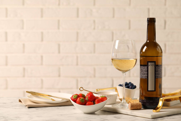 Bottle of wine, glass and delicious snacks on white marble table - Valokuva, kuva