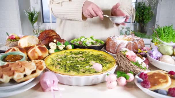 Vrouw bereidt feestelijk diner, Pasen brunch. Traditionele paasgerechten op familietafel - gebakken vlees, quiche, voorjaarsalade, muffin, gekleurde eieren, warme kruisbroodjes - Video