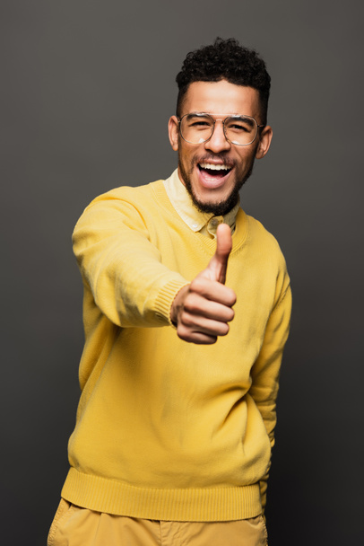 excited african american man in yellow outfit and glasses showing thumb up isolated on grey - Foto, Imagen