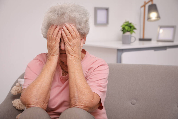 Senior woman with headache sitting on sofa at home. Space for text - Фото, зображення