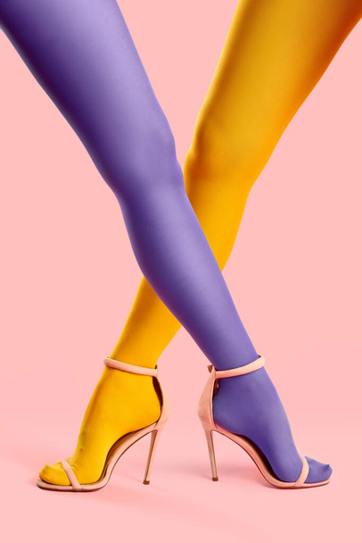 Long slim crossed legs of young women in yellow and purple tights posing on pink background - Fotó, kép